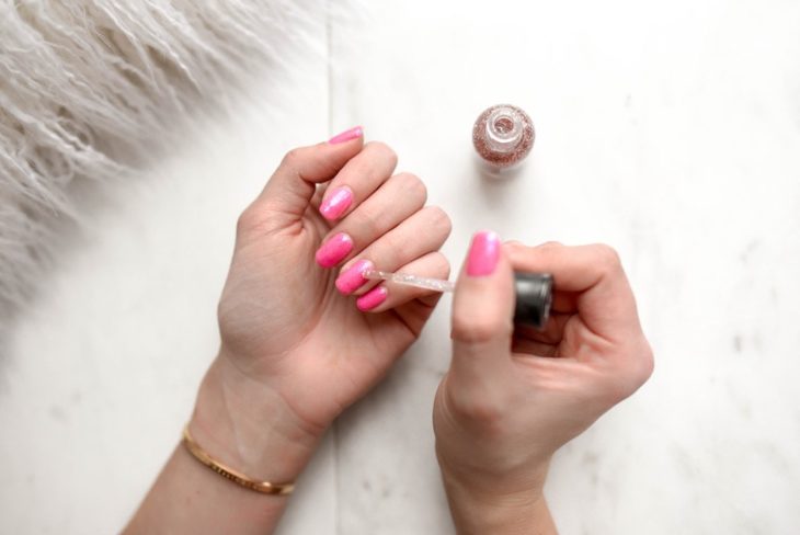 Chica pintando sus uñas con esmalte rosa 