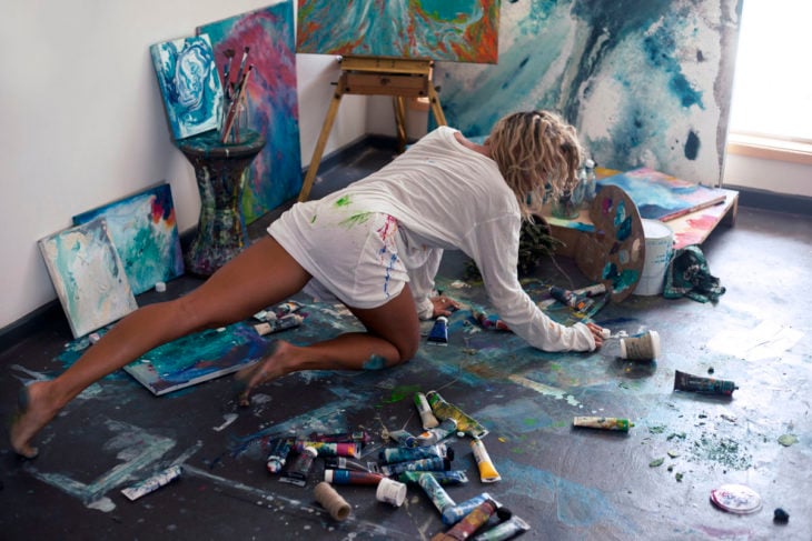 Chica sobre un piso de madera lleno de pintura de oleo, pintando