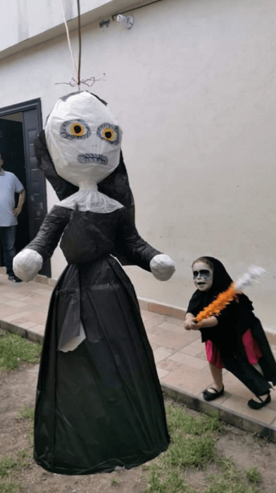 Niña disfrazada de monja quebrando una piñata del personaje de La Monja