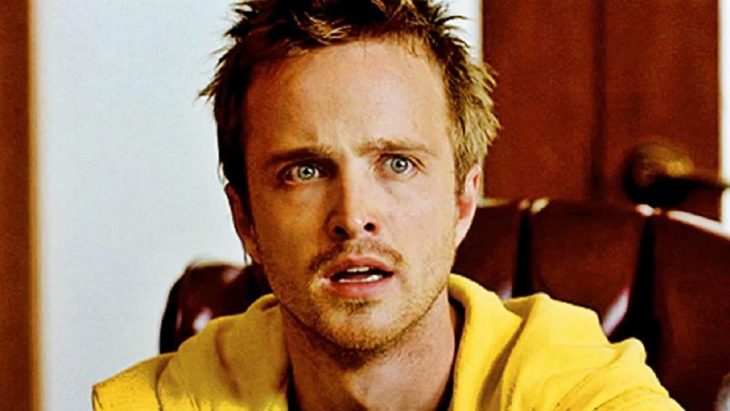 Jesse Pinkman sentado en una silla frente a un comedor, sorprendido, escena de la serie Breaking Bad