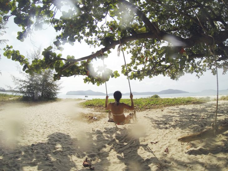 una chica se pasea en un columpio que pende de un árbol frente a la playa