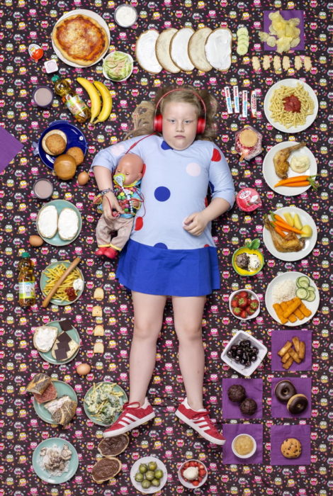Niña recostada en una alfombra morada, rodeada de comida, proyecto fotográfico de Gregg Segal