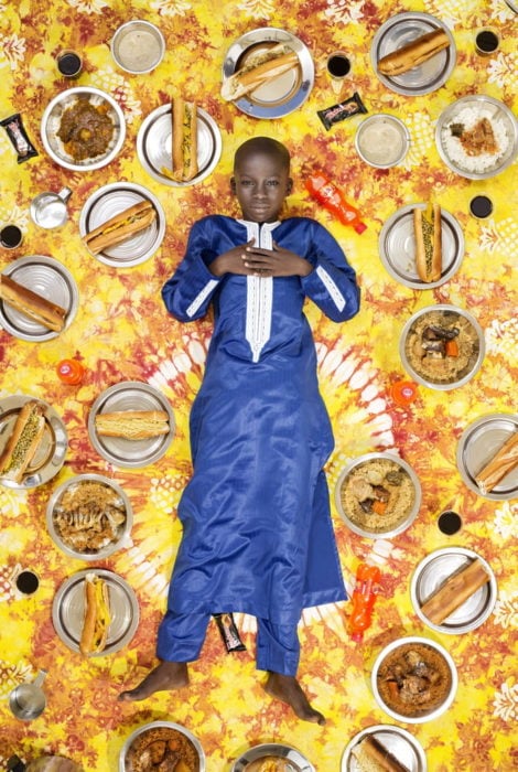 niño con ropa azul marino, recostado en el piso, rodeado de comida, proyecto fotográfico de Gregg Segal