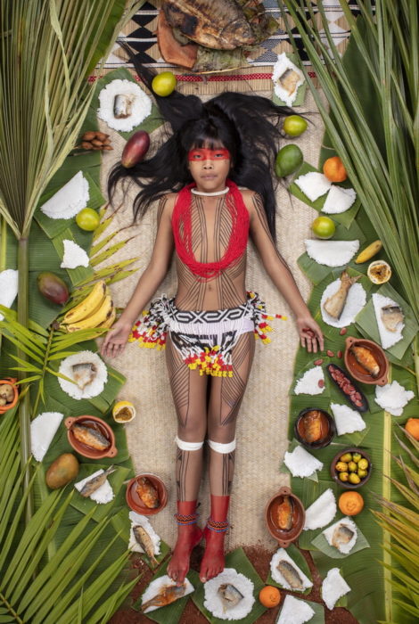 Niña con maquillaje en el rostro, recostada en el piso, rodeada de comida, proyecto fotográfico de Gregg Segal