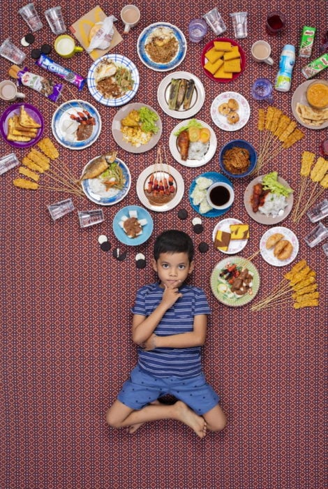 Chico recostado en el piso, rodeado de comida sobre su cabeza, proyecto fotográfico de Gregg Segal