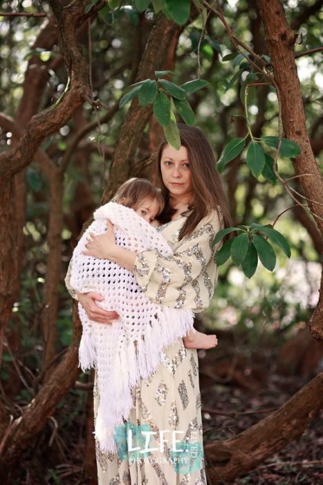 Elora Viano fotografiando a una madre cargando a su bebé mientras usa un vestido amarillo con lentejuelas 