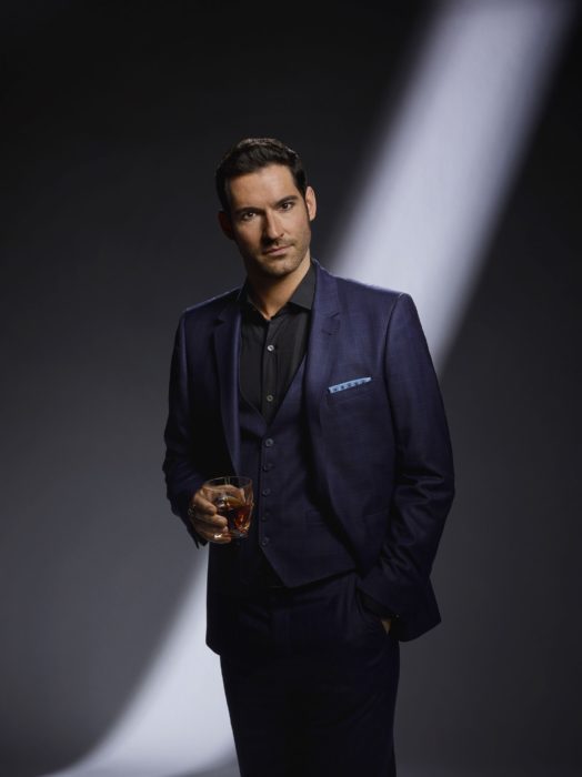 Actor de serie de Netflix, Lucifer, Tom Ellis; hombre sosteniendo un vaso, usa traje azul marino