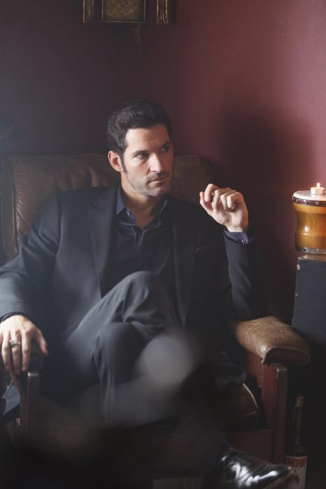 Actor de serie de Netflix, Lucifer, Tom Ellis; hombre con traje sentado en un sillón con las piernas cruzadas