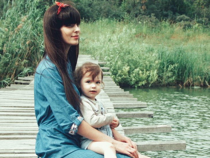 Las tías son como segundas mamás para los sobrinos; chica joven con paliacate en la cabeza y cabello largo y lacio con fleco; cargando a bebé a la orilla de un río