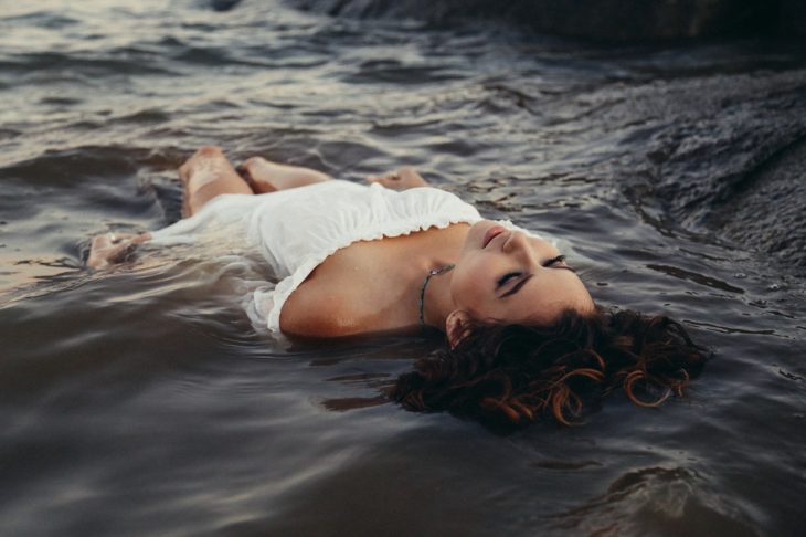 una mujer vestida de blanco acostada en la playa entre el agua