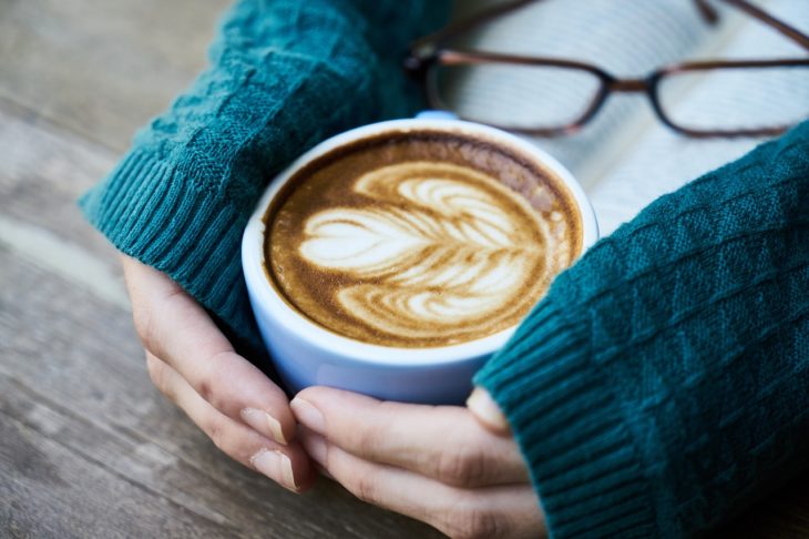 unas manos de mujer con un suéter azul abrazan una taza de café