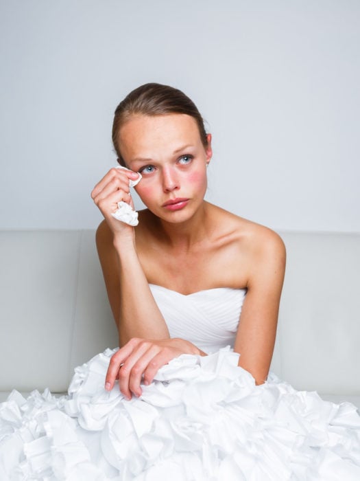 una joven vestida de novia sentada se limpia una lágrima con un pañuelo desechable