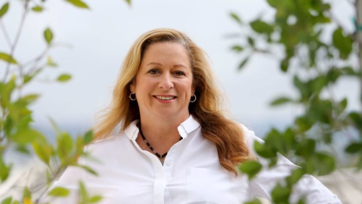 Abigail Disney con blusa blanca entre hojas de un árbol