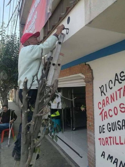 Señor de 79 años pintando un local de comida mientras está sobre una escalera metálica 