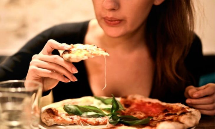 parte del viso di una donna che mangia pizza