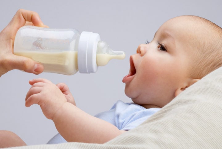 un bebé abre la boca mientras le acercan una mamila con leche