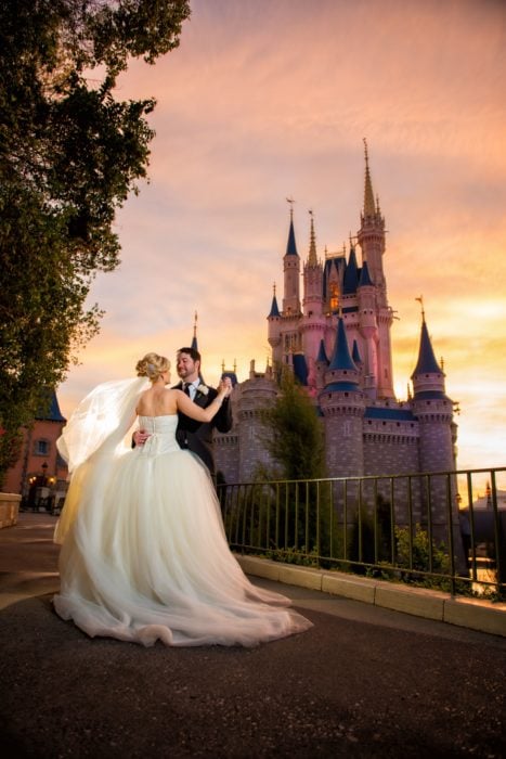 Precios de boda en Disneylandia; pareja de recién casados bailando frente al castillo de princesa de parque de diversiones