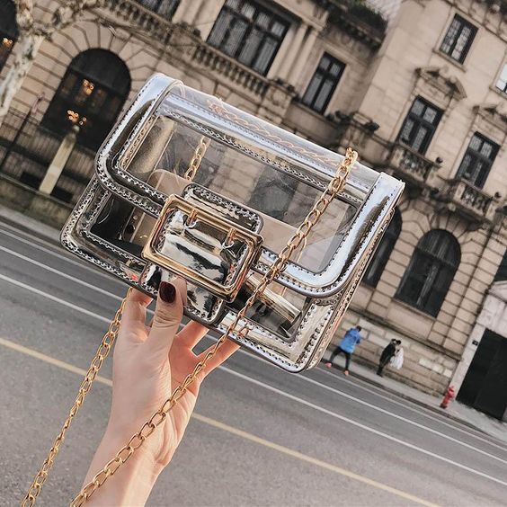 Mano de mujer sosteniendo bolso transparente pequeño con detalles en plateado