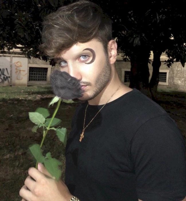 Stefan James, maquillista sosteniendo una rosa negra mientras enseña su ceja maquillada en forma de media luna 