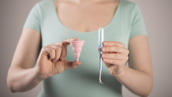 cuerpo de una mujer que sostiene de un lado la copa menstrual y de otro un tampón