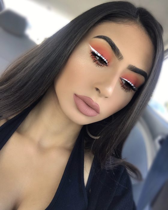 Chica con un delineado de color blanco sobre sus sombras de color naranja 