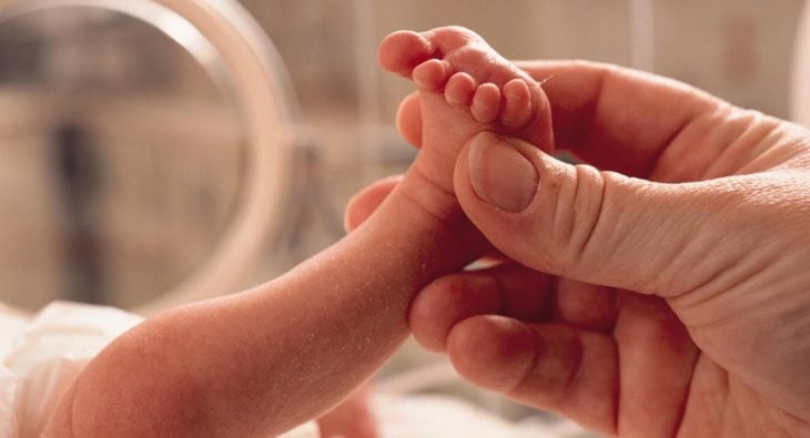 una mano de mujer sostiene un pie de un bebé prematuro