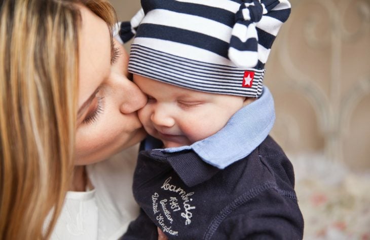 una mamá besa a su bebé con gorro azul con blanco