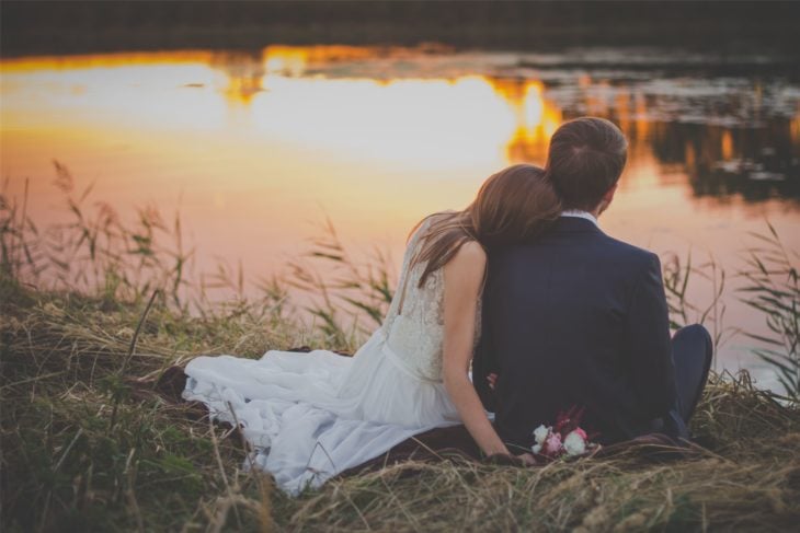 Sesión de fotos de boda; pareja de recién casados sentados junto a un lago