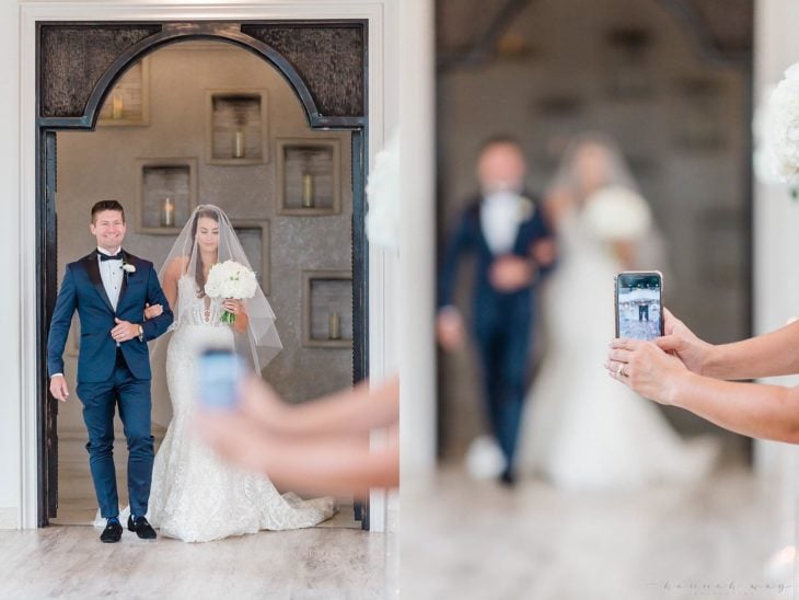 Fotógrafa de bodas Hannah Mbalenhle Stanley; novia con su vestido blanco de la mano de su papá entrando a la iglesia, chica se atraviesa con su teléfono para tomar foto