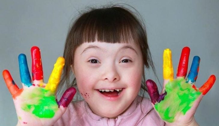 una niña con síndrome de Down muestra sus manos pintadas de colores