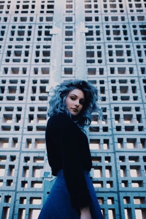 Chica modelando frente a un edificio, mostrando su cabello azul cielo