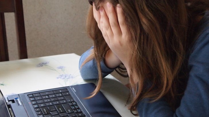 una mujer frente a una computadora se tapa la cara con las manos