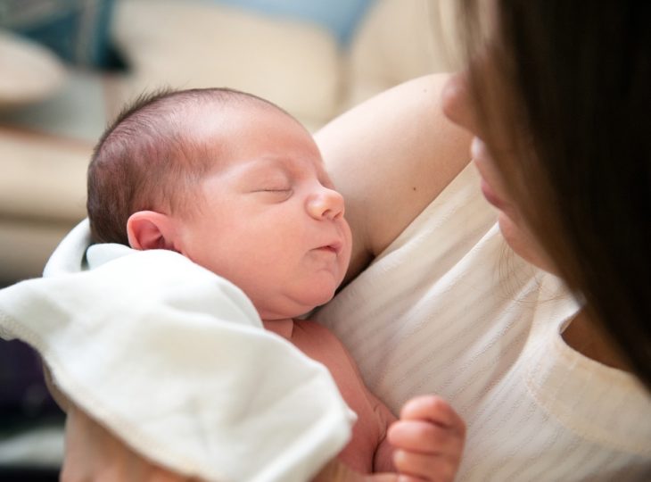 una mujer de pelo castaño y blusa beige con su bebé dormido sobre uno de sus brazos, toma picada