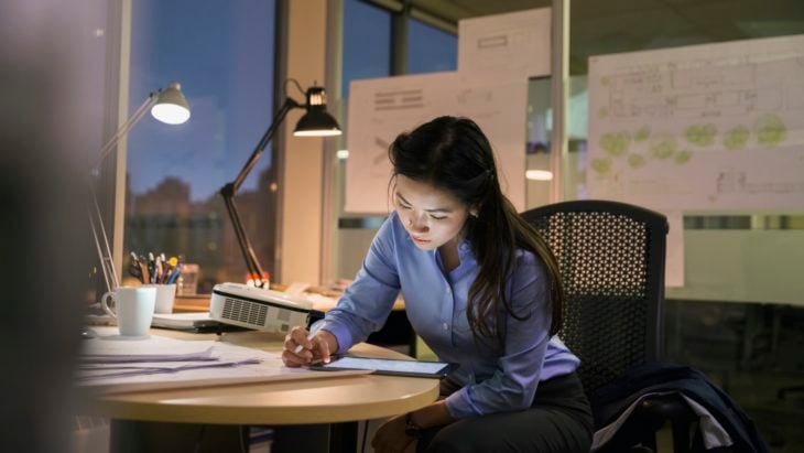 una joven de cabello largo y blusa azul trabaja de noche en una oficina