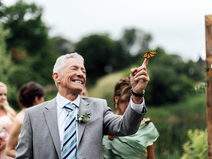 Hombre en un jardín sosteniendo una mariposa monarca en su dedo indice 