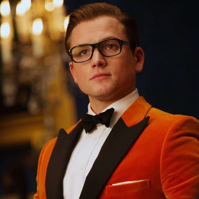 Taron Egerton vestido con saco rojo y moño negro, con lentes