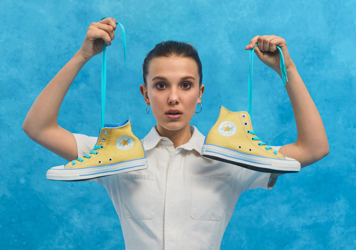 Millie Bobby Brown sosteniendo un par de tenis converse en color amarillo