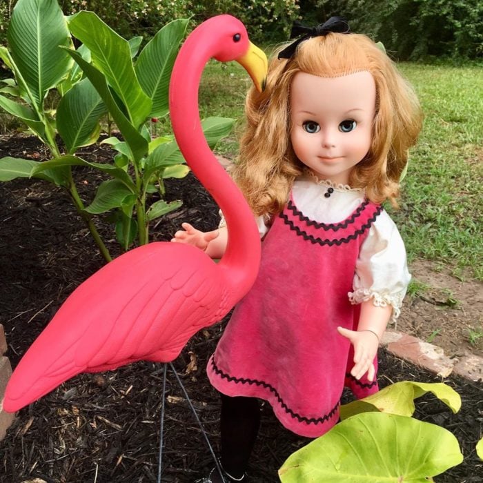 Madeline y Malachi Dressel; muñeca vintage con vestido rosa y cabello rubio en el jardín junto a un flamenco de adorno