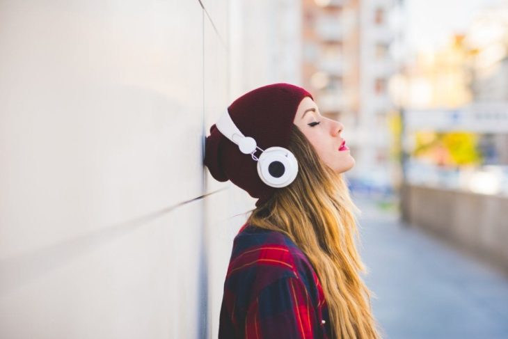 chica rubia cerrando los ojos recargada en la pared escuchando música en audífonos