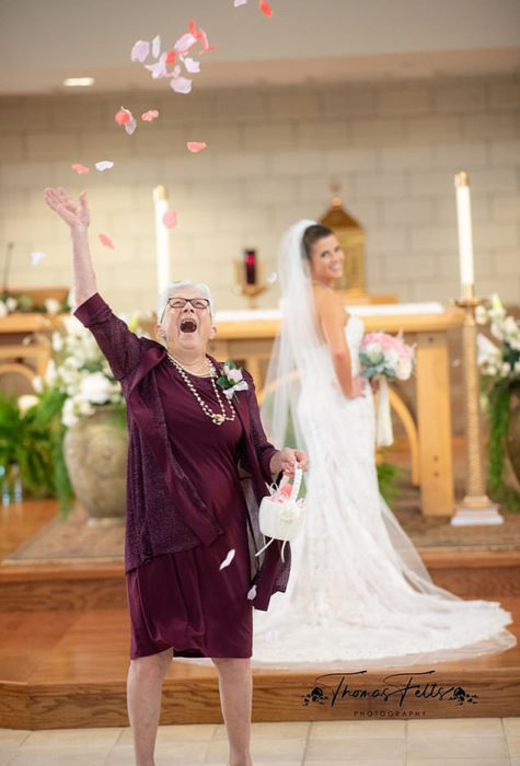 Abuela lanzando pétalos mientras su nieta está posando para las fotos de su boda 