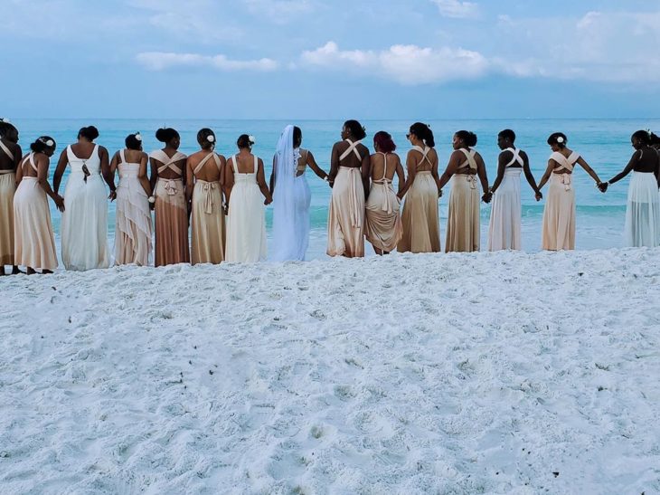 Novia posando junto a sus 34 damas de honor el día de su boda en la playa, vestidas en color nude 