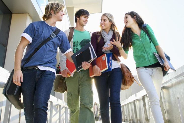 un grupo de cuatro estudiantes adolescentes caminando por un pasillo