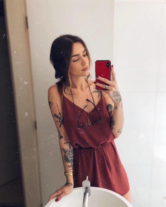 Chica tomándose selfie frente al espejo, con vestido de verano color rojo; con tatuajes en los brazos