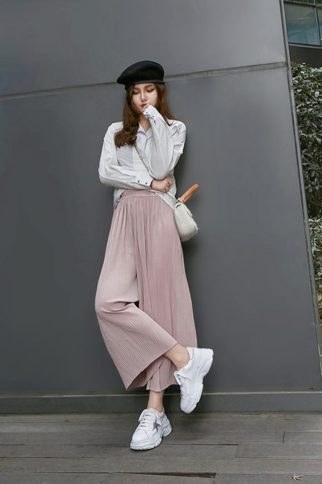 Chica usando un pantalón culotte de color rosa palo con blusa blanca, boina francesa y tenis ugly en color blanco 