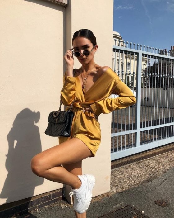 Chica usando un jumpsuit de seda color amarillo con unos tenis ugly de color blanco 