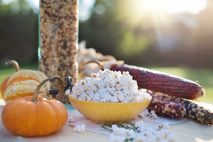 palomitas de maíz en un plato amarillo al lado de unas mazorcas de maíz sobre una mesa