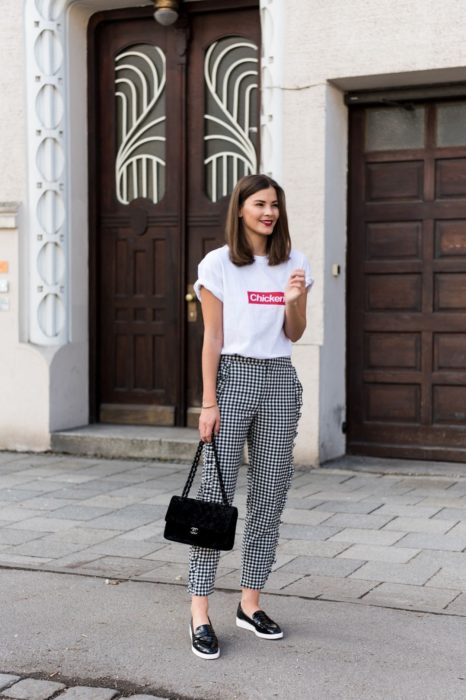 Chica usando un pantalón de cuadros negro con gris y una camisa de color blanco 