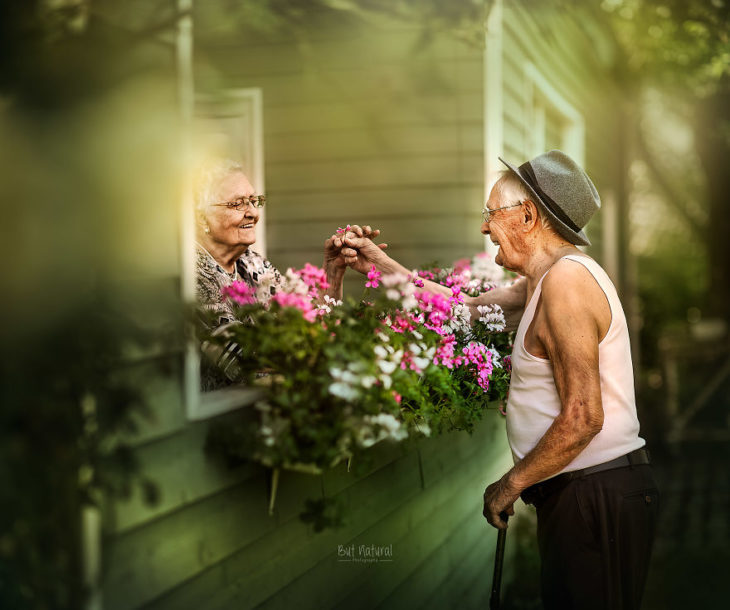 Abuelos platicando a través de una ventana rodeada de flores, fotografía de Sujata Setia