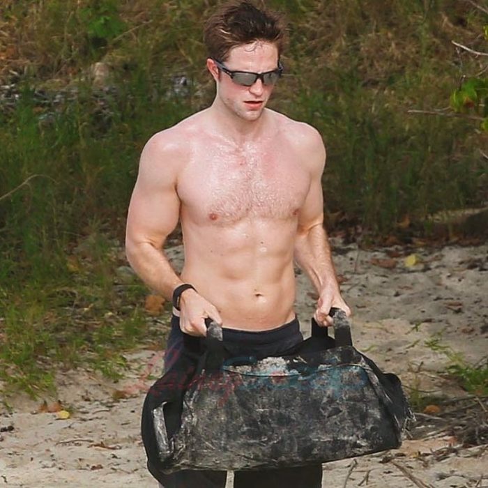 Robert Pattinson entrenando en la playa mientras carga un costal con piedras 