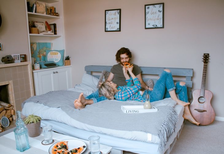 una pareja en una cama come pizza